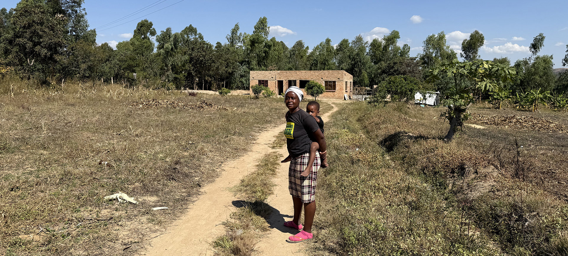 Margaret and her child stand outside the house that she and her husband have managed to build since growing their business with the support of MicroLoan Foundation